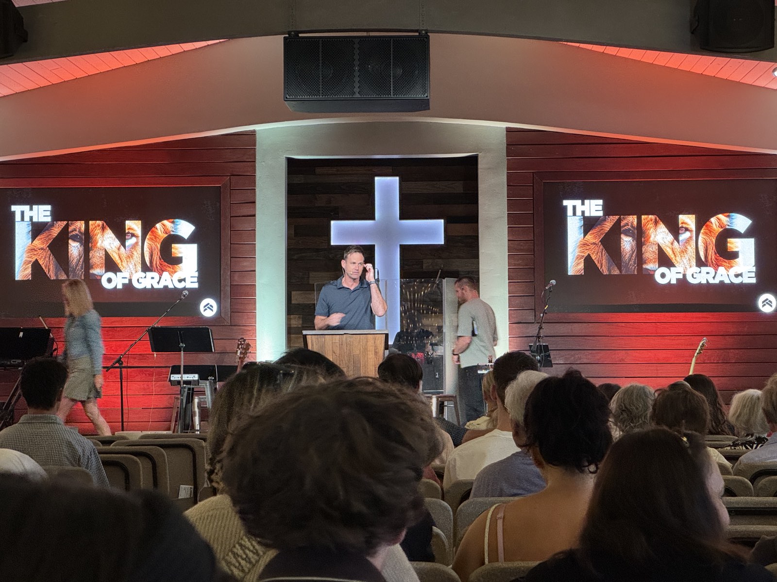 Pastor preaching at Agoura Bible Fellowship between two LED screens showing sermon graphics, with the stage evenly lit