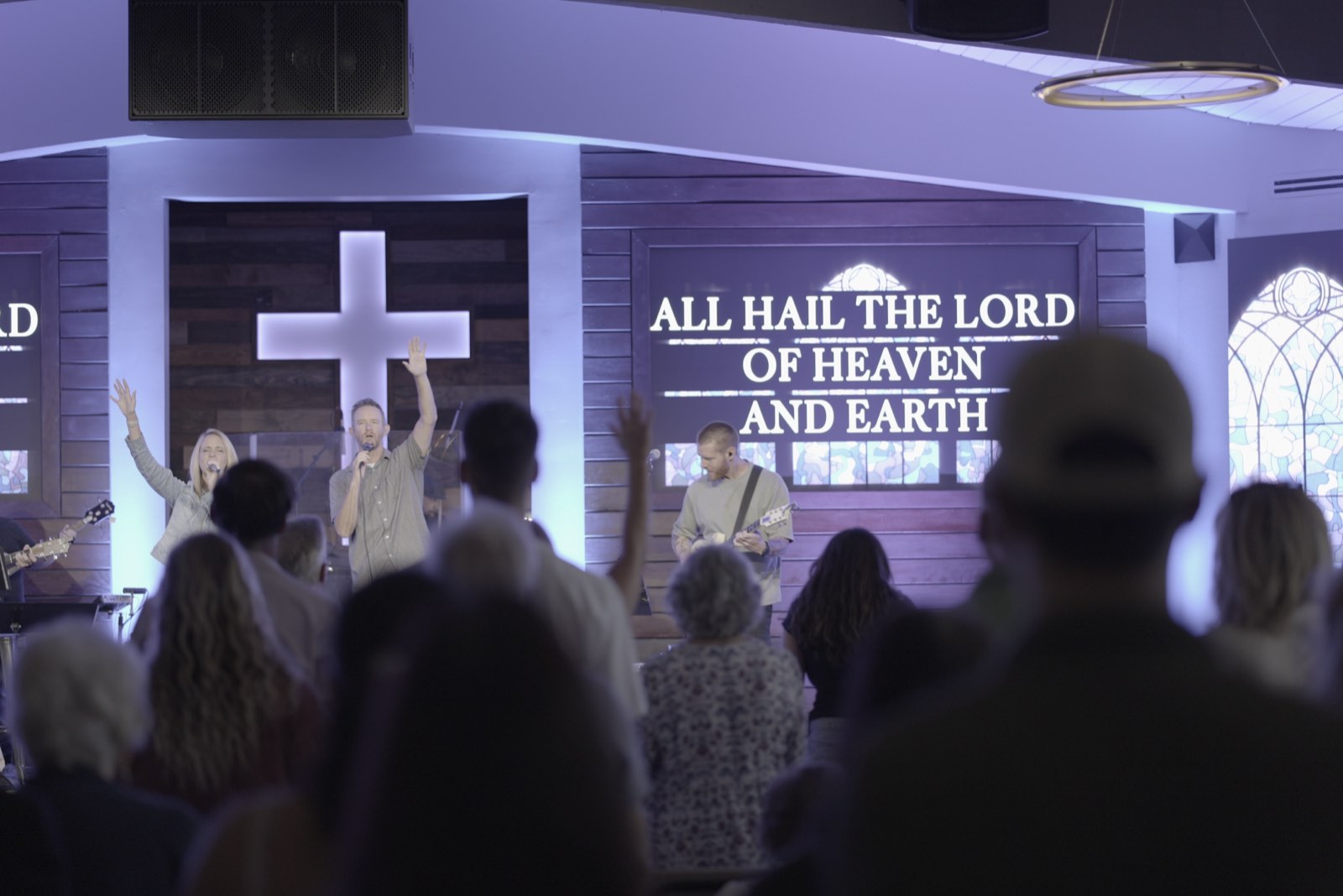 Congregation raising hands in worship at Agoura Bible Fellowship with lyrics on the LED screens