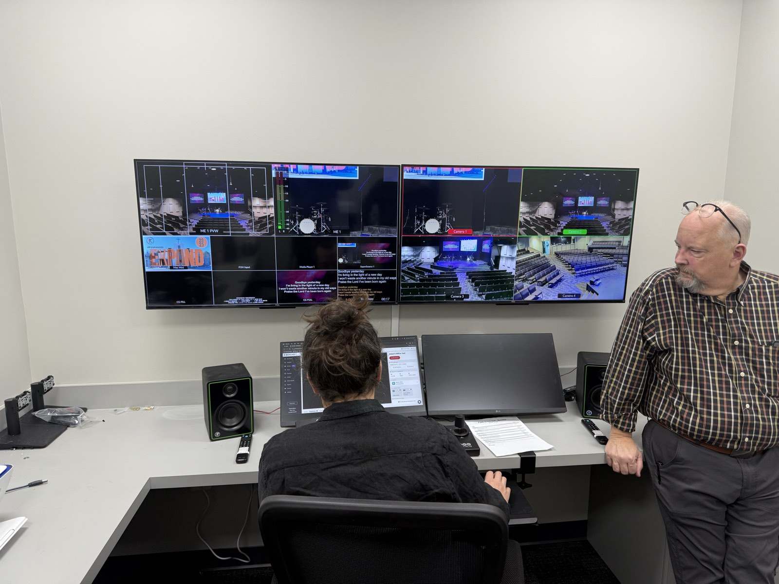 Two people at the broadcast control room desk in front of a multiview video wall at Faith Covenant Church of God