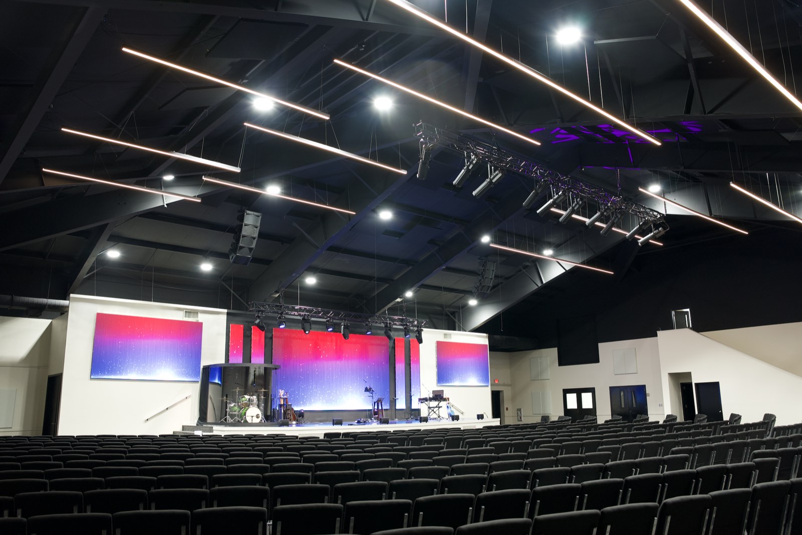 First Baptist Church Pontotoc worship center, a converted gymnasium, with rows of chairs, linear house lights, lighting truss and LED walls on stage
