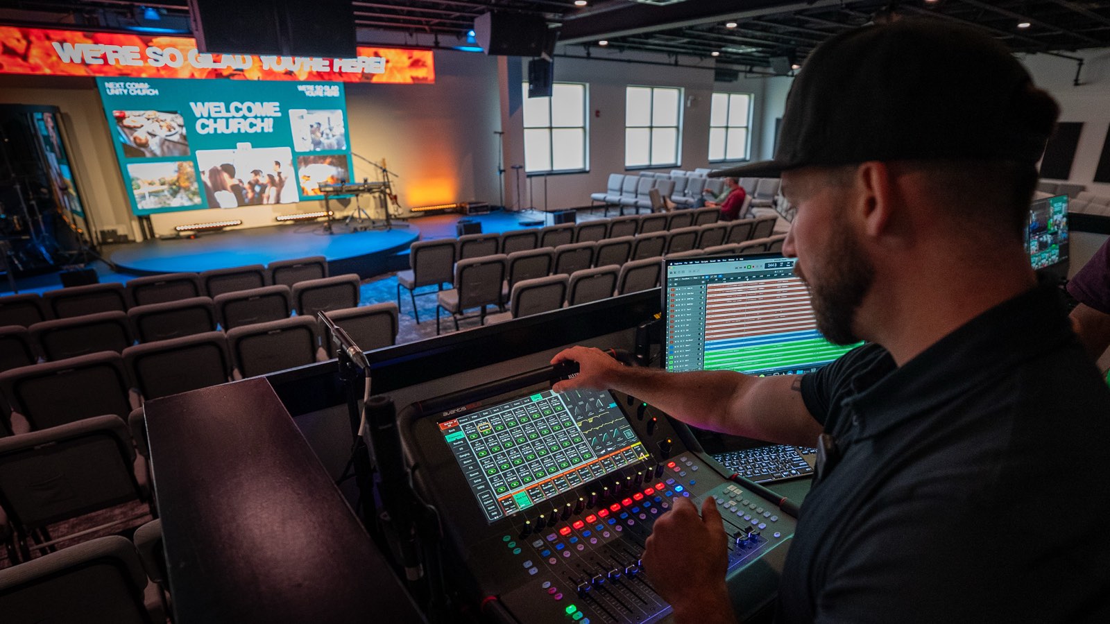 Volunteer at the Next Community Church front of house console with the lyric banner and center LED screen showing a welcome slide