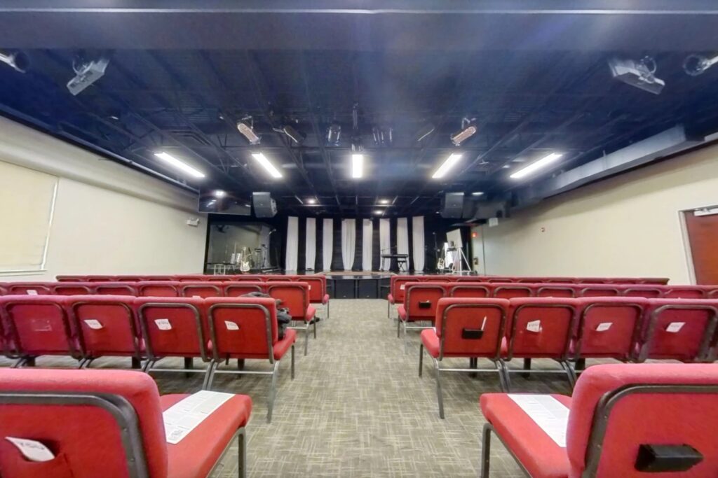 The Next Community Church auditorium before the Churchfront installation, looking down the centre aisle at red stacking chairs and a bare platform