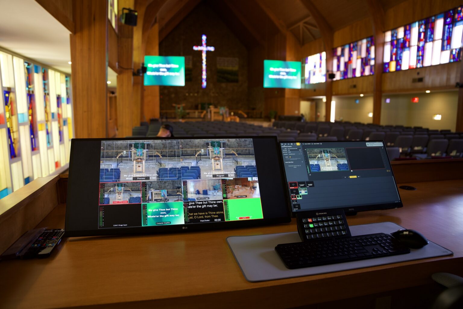 Clean church tech booth with KVM screens and a single keyboard facing a sanctuary with stained glass