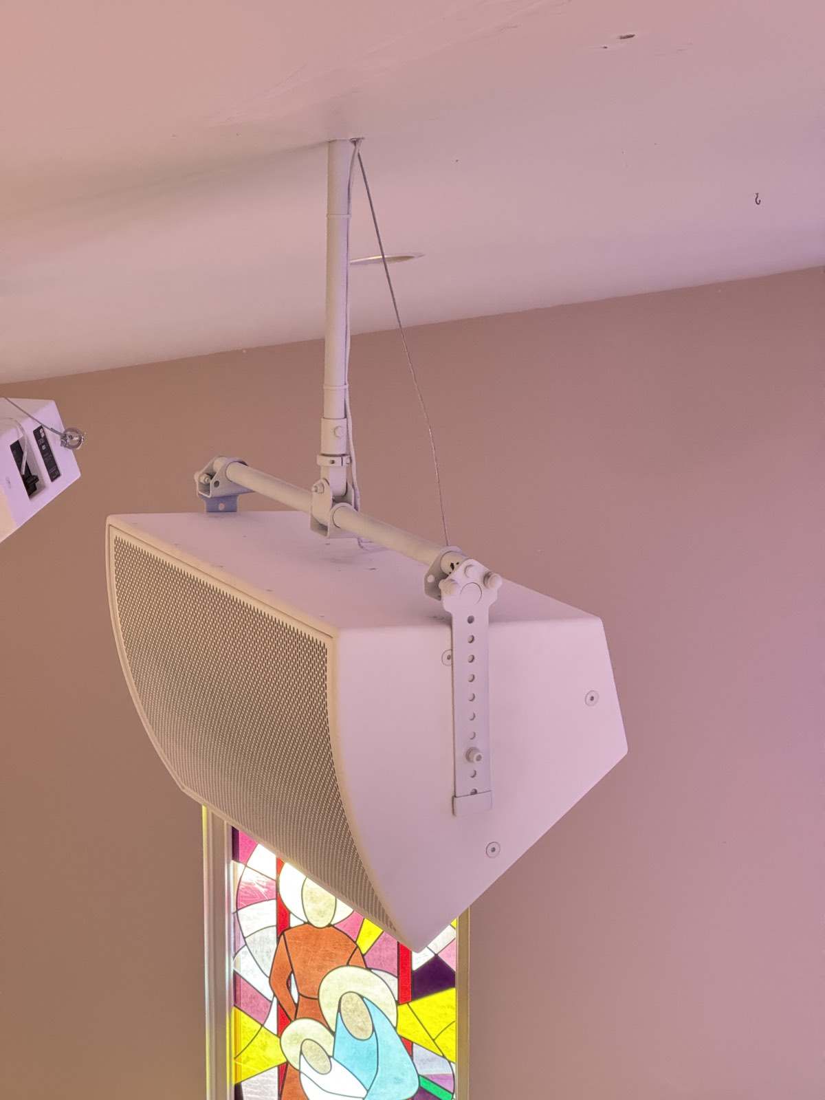 White Fulcrum Acoustic speaker hung from the ceiling beside a stained glass window at Trinity Church