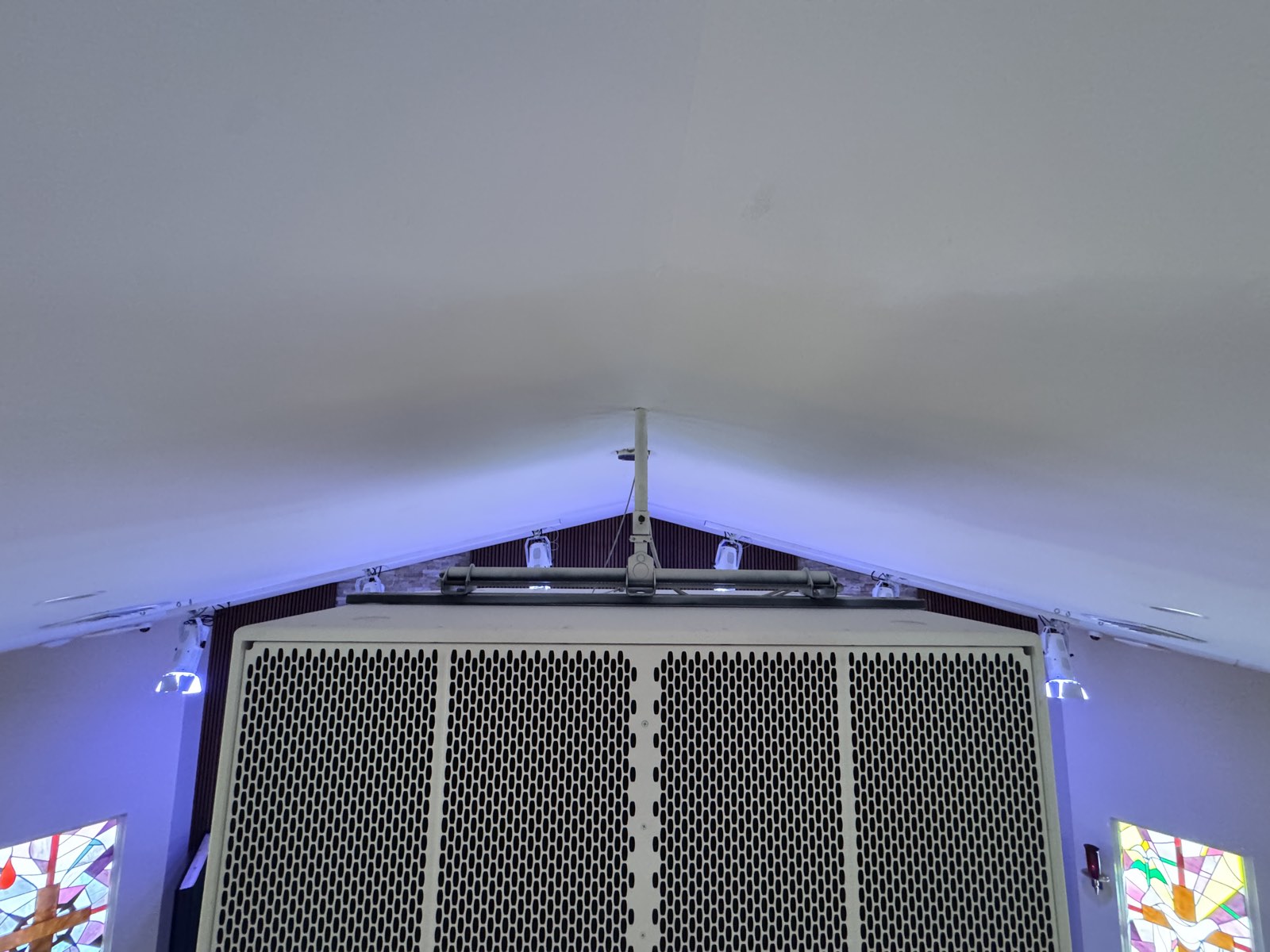 White dual 18-inch subwoofer cabinet flown at the ceiling peak of the Trinity Church sanctuary