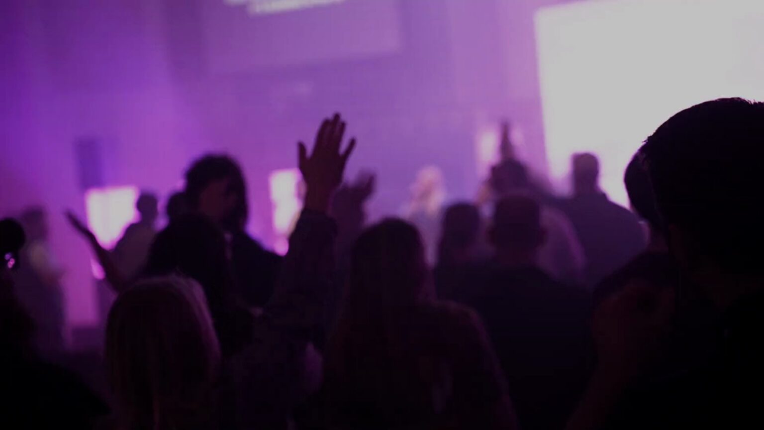 Attendees with hands raised in worship under purple light at the Churchfront Conference